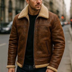 Op de afbeelding: Bruine leren jas met een crèmekleurige schapenvachtkraag en manchetten. De jas heeft een ritssluiting en een klassiek ontwerp. Het model draagt een zwart shirt en een blauwe jeans. Een stijlvol bovenkledingstuk.