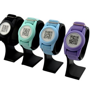 May include: Four wristbands with circular centers featuring a black and white QR code. The bands come in black, mint green, light blue, and purple, each with a matching circular frame and a metallic adjustment buckle on the fabric strap.