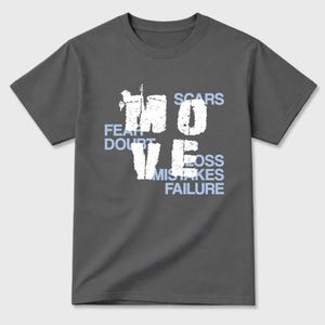 May include: Dark gray t-shirt with the word "MOVE" in large, distressed white letters. Below the word are the words "FEAR, DOUBT, MISTAKES, FAILURE" in light blue. The word "SCARS" and "LOSS" are also in light blue.