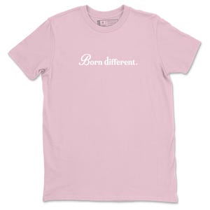 Op de afbeelding: Lichtroze t-shirt met de witte tekst "Born different." in een cursief lettertype. Het shirt heeft korte mouwen en een ronde hals. De stof lijkt zacht.