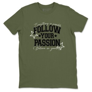 Könnte beinhalten: Olivgrünes T-Shirt mit dem Text "Everything is possible, Follow Your Passion, Believe in yourself" in Schwarz und Weiß. Das Design enthält Sterne. Das T-Shirt hat kurze Ärmel und einen Rundhalsausschnitt.