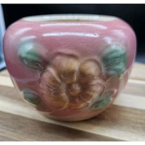 May include: A small, round, pink ceramic bowl with a floral design. The bowl has a crackled glaze and a light pink interior. The floral design features a central flower with green leaves. The bowl is likely for decorative purposes.