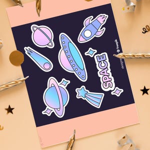 Könnte beinhalten: Ein Bogen mit Aufklebern zum Thema Weltraum mit Planeten, Raketen, einem Kometen und einem UFO in Pastellfarben. Das Wort "SPACE" ist weiß geschrieben. Die Aufkleber befinden sich auf einem dunkelblauen Hintergrund mit einem rosa Rand.
