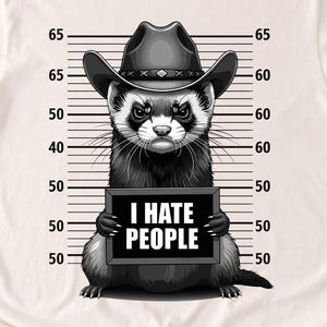 May include: Cream-colored t-shirt featuring a black and white illustration of a ferret wearing a cowboy hat and holding a sign that reads "I HATE PEOPLE." The shirt is paired with blue jeans and white sneakers.