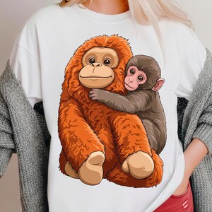 Könnte beinhalten: Weißes T-Shirt mit einer Cartoon-Illustration eines großen, orangefarbenen Orang-Utans, der einen braunen Baby-Orang-Utan umarmt. Der Text "PNG DIGITAL DOWNLOAD" befindet sich am unteren Rand des Bildes. Geeignet für den digitalen Download.