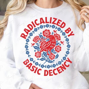 Könnte beinhalten: Weißes Sweatshirt mit einem rot-blauen Blumendesign und dem Text "RADICALIZED BY BASIC DECENCY". Das Design zeigt einen roten Vogel, umgeben von Blumen und Blättern. Der untere Teil des Bildes lautet "3 Color Variations - High Quality PNG".