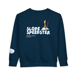 Op de afbeelding: Marineblauwe sweatshirt met de tekst "SLOPE SPEEDSTER" in witte letters, samen met een illustratie van ski's en stokken. De sweatshirt heeft ook de tekst "HARLAND HOME CO EST. 2015" en een kleine skibrilafbeelding op de mouw.