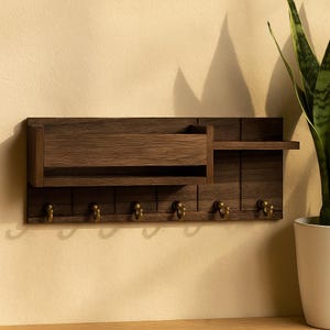 Könnte beinhalten: Ein dunkelbrauner Wandorganizer aus Holz mit einem Regal, einem Postfach und sechs messingfarbenen Haken. Der Organizer ist für den Eingangsbereich oder das Büro konzipiert.