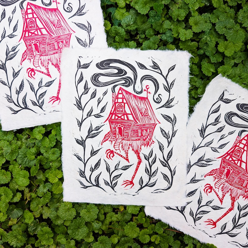 May include: Three art prints featuring a red and white house with chicken legs, surrounded by black foliage. The house has a chimney with smoke and is set against a white background. The prints are on textured paper.