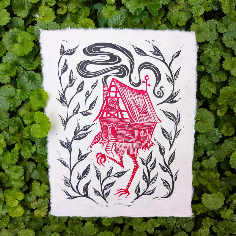 May include: A red and black linocut print of a whimsical house with chicken legs, a smoking chimney, and an eye on the facade. The house is surrounded by black leafy vines on a white background.