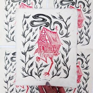 May include: A red and black linocut print of a whimsical house with legs, surrounded by leafy vines. The house has a chimney with swirling smoke and an eye symbol. The print is on textured, off-white paper.