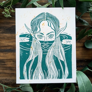 May include: A teal blue linocut print of a woman with long hair and pointed ears. The woman's face is partially obscured by a mask. The background is a teal blue with white stars.