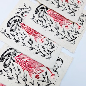 May include: A collection of linocut prints featuring a red and black design. The prints showcase a stylized creature with a house-like form, intertwined with leafy branches and swirling black shapes. The prints are on textured, off-white paper.