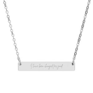 Puede incluir: Un collar plateado con una cadena delicada y un colgante rectangular. El colgante lleva grabada la frase "I have been changed for good" en cursiva. El collar se muestra sobre un fondo blanco.
