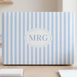May include: A laptop skin featuring a vertical light blue and white striped pattern. In the centre, there is a white oval with a scalloped edge containing the blue capital letters MRG. The design covers the entire rectangular surface of the laptop.