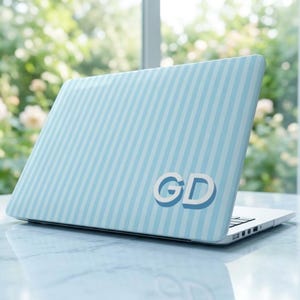 May include: A laptop computer featuring a light blue and white vertical striped skin on the outer lid. The letters GD are displayed in a bold, white, sans-serif font with a subtle blue drop shadow on the lower right side of the laptop cover.