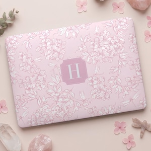 May include: A rectangular laptop skin featuring a light pink background with a white floral and dragonfly pattern. In the center, a solid pink rectangular frame with clipped corners contains the white capital letter H as a monogram.