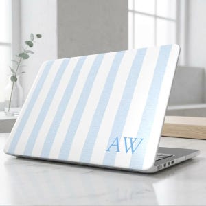 May include: A laptop skin featuring a pattern of vertical light blue and white stripes. The bottom right corner of the laptop lid displays the personalized capital letters AW in a light blue serif font, matching the color of the stripes.