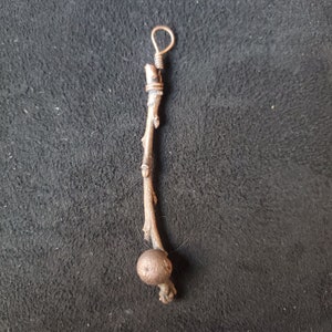 May include: A brown twig pendant with a copper wire loop at the top and a copper ball at the bottom.