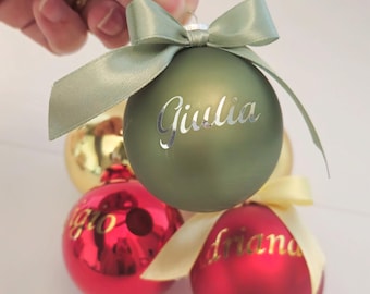 Könnte beinhalten: Eine Auswahl an Weihnachtskugeln in Grün, Rot und Gold. Die grüne Kugel trägt den Namen "Giulia" in silberner Schrift und ein grünes Band. Andere Kugeln haben Namen in goldener Schrift. Festliche Dekorationen.