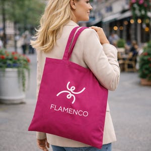 Könnte beinhalten: Eine magentafarbene Tragetasche mit weißem Text und einem stilisierten Design. Das Wort "FLAMENCO" ist in Weiß unter dem Design aufgedruckt. Die Tasche hat zwei Henkel und wird über der Schulter getragen.