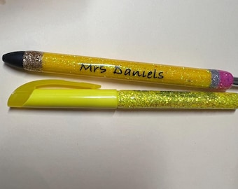 May include: Two writing instruments: a yellow pen with glitter accents and the text "Mrs. Daniels", and a yellow highlighter with glitter. Both have black and silver tips. The pen has a pencil-like design.