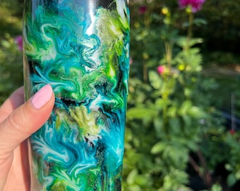 May include: A tumbler with a black lid and a swirling design in shades of green, blue, and white. The design resembles a marbled effect. The tumbler is cylindrical and appears to be made of a glossy material.