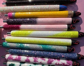 May include: A collection of glitter pens in various colors, including blue, silver, black, yellow, pink, and green. Each pen has a silver tip and a black or blue end. The pens are arranged in a neat, parallel row.