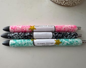 May include: Three pens with glittery barrels in pink, black, and teal. Each pen features a white label resembling a composition book cover with the text "COMPOSITION BOOK" and "100 Sheets - 200 Pages Wide Ruled" and gold star accents.