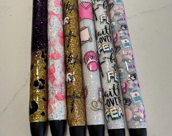 May include: A collection of six glitter pens with various designs. The pens feature black ink tips and silver tops. Designs include leopard print, pink bows, gold crosses, and the words "Faith Over Fear" with medical-themed patterns.