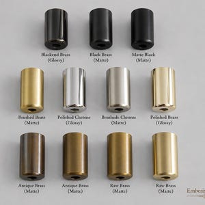 May include: A collection of eleven cylindrical metal hardware components arranged in three rows. The finishes include Blackened Brass, Black Brass, Matte Black, Brushed Brass, Polished Chrome, Brushed Chrome, Polished Brass, Antique Brass, and Raw Brass.