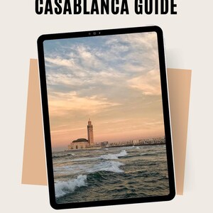 May include: A digital tablet shows a scenic view of Casablanca, Morocco, with the text "CASABLANCA GUIDE" at the top. The image shows a mosque by the ocean under a sunset sky. The text "EXPLORE CASABLANCA LIKE A LOCAL" is at the bottom.