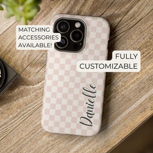 Puede incluir: Funda de teléfono con un patrón de cuadros rosa y blanco. El nombre "Danielle" está escrito en cursiva. También se ven los textos "Matching Accessories Available!" y "Fully Customizable".