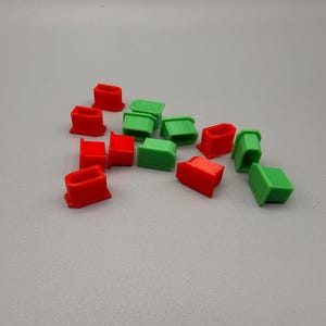 May include: A collection of small, rectangular, plastic objects in red and green. The objects are scattered across a gray surface. The shapes appear to be caps or covers, possibly for a larger item.