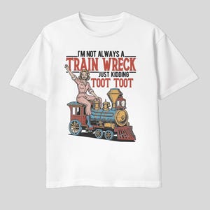 May include: White t-shirt featuring a colorful graphic of a woman riding a vintage train. The text reads "I'm not always a train wreck, just kidding, toot toot" in red and black. The design is a playful, retro style.