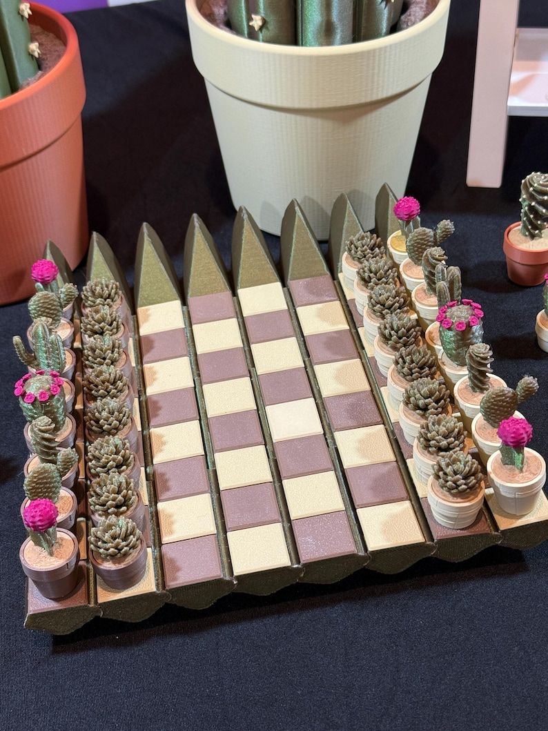 May include: A display of miniature cactus plants in small pots, arranged on a decorative, geometric platform. The cacti feature various shapes and are adorned with pink flowers. The platform has a brown and beige checkered pattern.