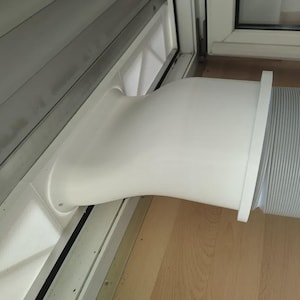 Puede incluir: Un kit de sellado de ventana de plástico blanco para aire acondicionado portátil, con un adaptador de boquilla plana conectado a una manguera de escape flexible y acanalada que se extiende hacia afuera del marco de la ventana.