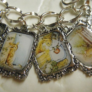May include: A silver charm bracelet with five charms featuring images of Peter Rabbit from the children's book series. The charms are silver with a white background and colorful illustrations.