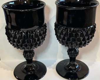 May include: A pair of black glass goblets featuring a smooth, flared rim and a textured, diamond-patterned bowl. The stem includes a small, matching diamond-textured decorative accent above a circular base, creating a cohesive, dark aesthetic.