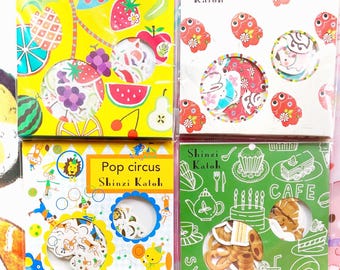May include: Four packs of decorative stickers. The top left pack has a yellow background with fruit illustrations. The top right pack has a white background with red floral and animal illustrations. The bottom left pack has a circus theme. The bottom right pack has a green background with cafe illustrations.