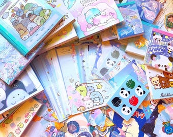 May include: A collection of colorful stationery items, including notebooks, stickers, and notepads. The items feature cute cartoon characters and pastel color schemes. The image has a bright and cheerful aesthetic, perfect for school or crafting.