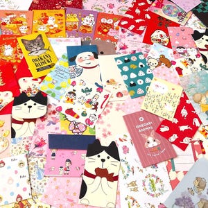 May include: A collection of colorful, illustrated cards and envelopes featuring various designs, including cats, bears, and floral patterns. Some cards have Japanese text. The assortment includes red, pink, and white backgrounds.
