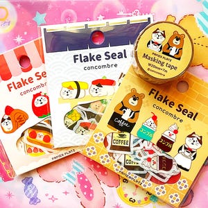 May include: An assortment of Japanese stationery items, including sticker packs and masking tape. The sticker packs feature cute illustrations of cats, bears, and food items. The masking tape roll has a cat and bear design. The text "Flake Seal concombre" is visible.