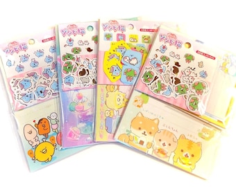 May include: A collection of colorful sticker packs featuring various cartoon characters and Japanese text. The stickers are packaged in clear plastic and include designs of cute animals, food, and other whimsical illustrations. The overall color scheme is pastel.
