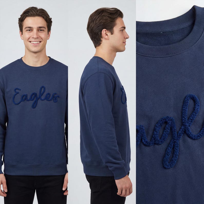 May include: A navy blue crew neck sweatshirt featuring the word "Eagles" embroidered in a darker blue, textured script. The sweatshirt is a solid colour and has a relaxed fit. The image shows the sweatshirt from multiple angles.