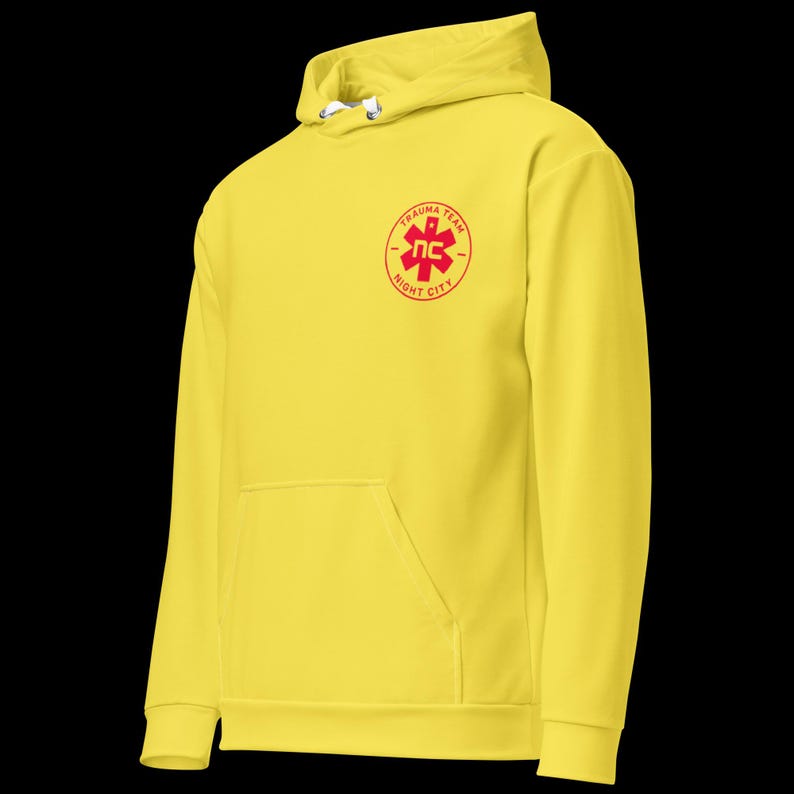 May include: A bright yellow hoodie with a front pocket and drawstring hood. The hoodie features a red circular emblem on the chest with the words "TRAUMA TEAM" and "NIGHT CITY" surrounding a stylized medical symbol.