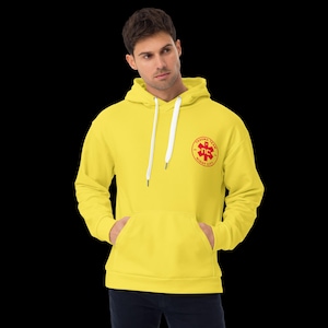 May include: A bright yellow hoodie with a front pocket and a drawstring hood. The hoodie features a red emblem with the words "TRAUMA TEAM" and "NIGHT CITY". The person is wearing dark pants.