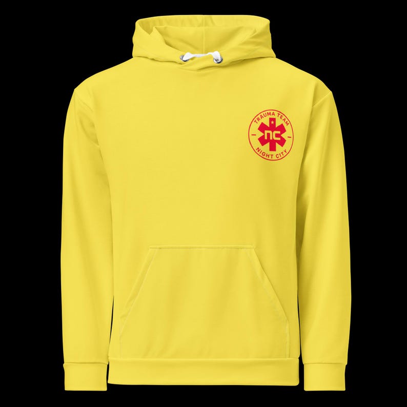 May include: Bright yellow hoodie with a front pocket and drawstring hood. The hoodie features a red emblem on the chest that reads "TRAUMA TEAM NC NIGHT CITY". The design is centered on the chest.