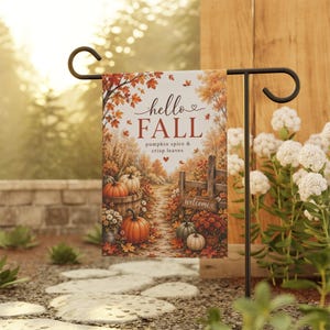 Puede incluir: Una bandera de jardín rectangular colgada en un soporte de metal negro, con una escena otoñal de calabazas, follaje y una valla de madera. El texto dice hello FALL, pumpkin spice & crisp leaves y welcome en un pequeño letrero de madera.