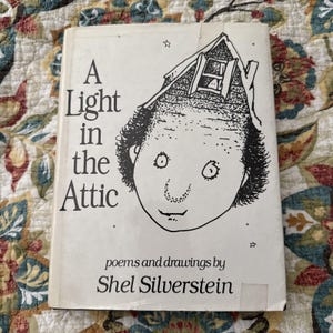 May include: A vintage copy of "A Light in the Attic" by Shel Silverstein. The book cover features a whimsical black and white illustration of a face with an attic for a head. The title is in large, bold letters.